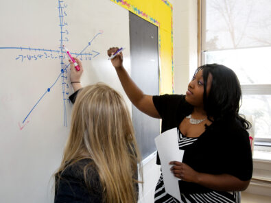 Teaching fellow and student solving math problem on whiteboard Knowles Teacher Initiative